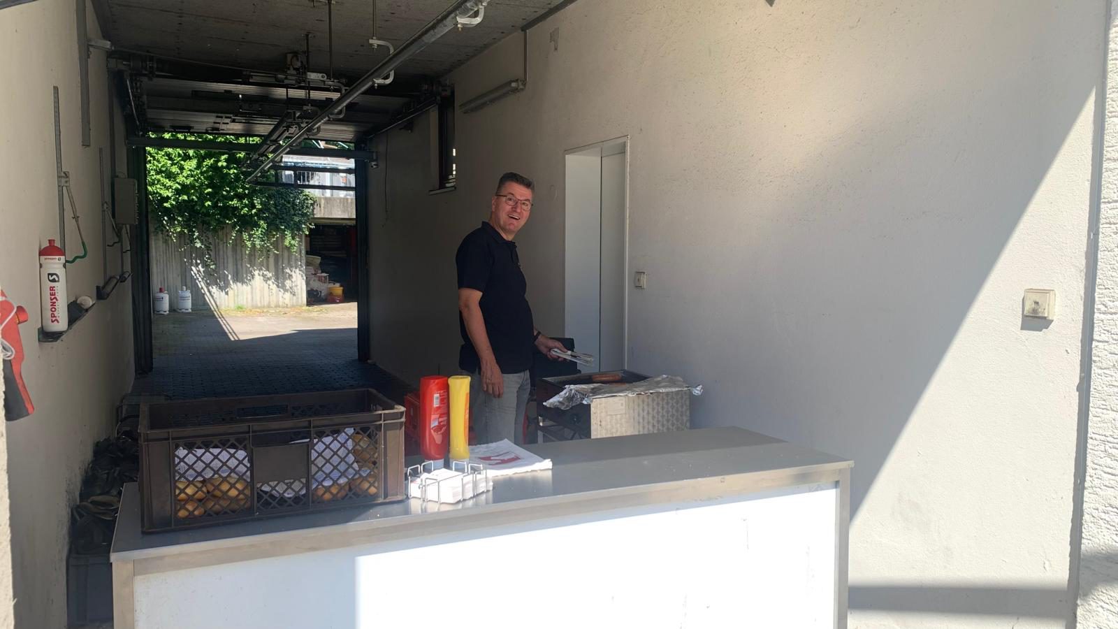 Der Grillstand bei der Metzgerei Schäfer in der Sonne, mit Würsten auf dem Grill, Brötchen, Ketchup und Senf