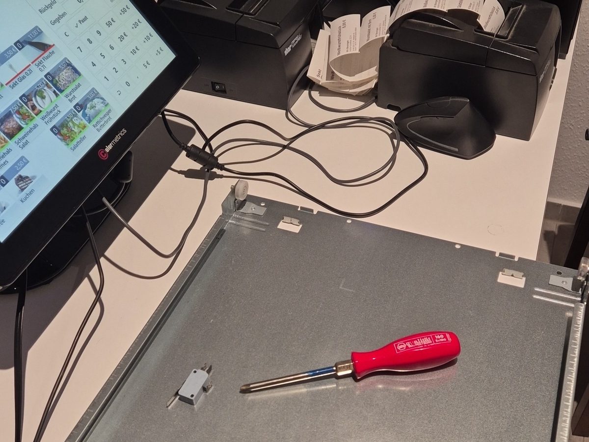 Kassenbildschirm mit Artikeln und Preisen, daneben die aufgeschraubte Geldschublade