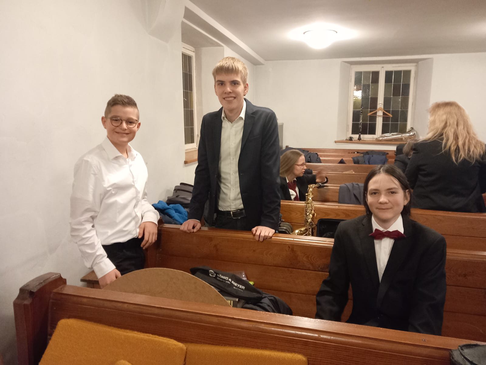 Drei junge Musiker in weißen Hemden vor einem bunten Kirchenfenster