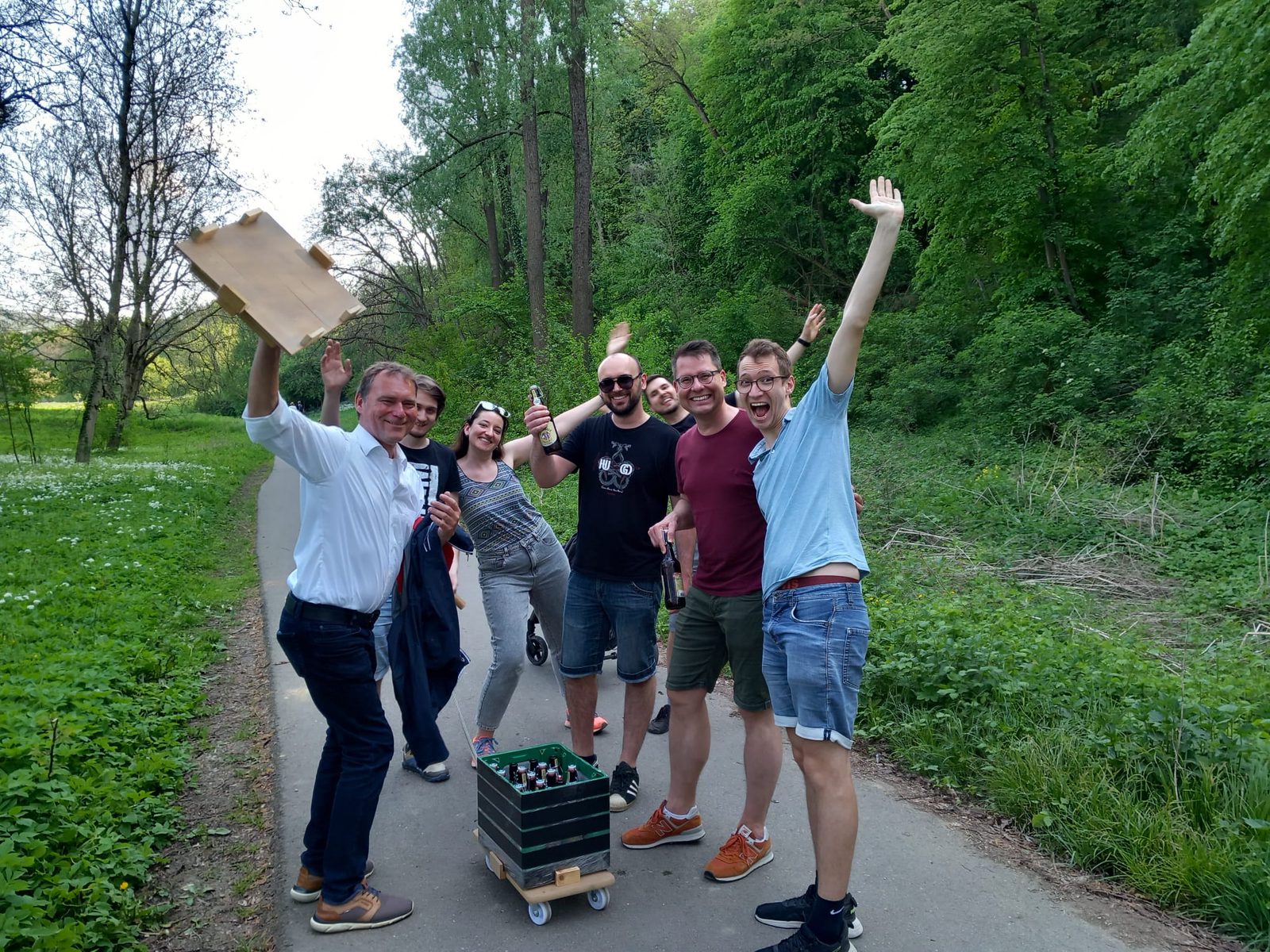 Die Wandergruppe jubelt auf einem Waldweg zwischen Bärlauch, vorn der Bollerwagen aus Getränkekisten