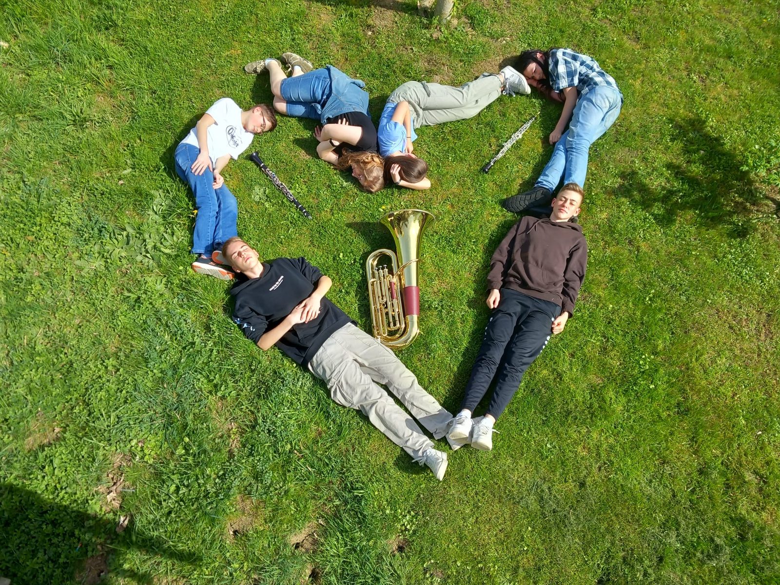 Sieben junge Musikerinnen und Musiker liegen mit ihren Instrumenten in Herzform im Gras