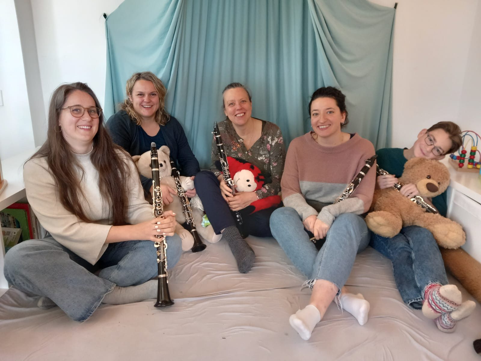 Fünf Klarinettistinnen und Klarinettisten sitzen mit Teddybären und Klarinetten auf einer Matratze