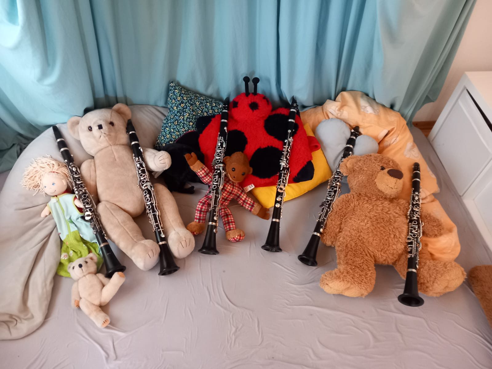 Sechs Klarinetten lehnen an Teddybären, einer Puppe und einem Marienkäfer-Kissen